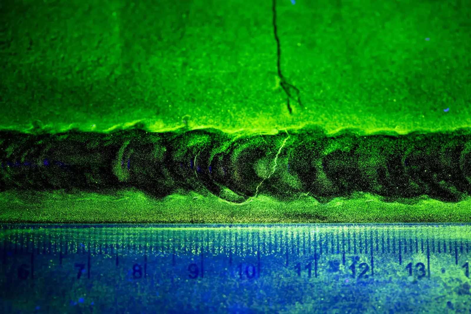 Fluorescent magnetic particle indication of a crack along a weld, next to a ruler